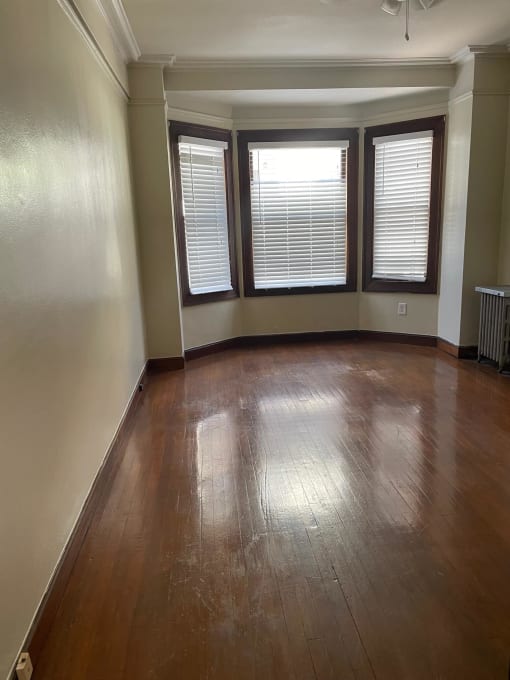 an empty living room with wooden floors and three windows